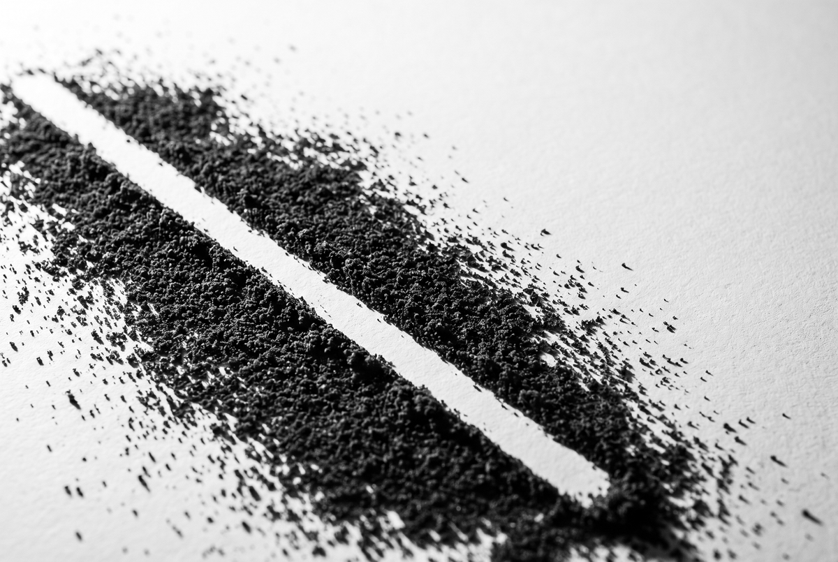 Poussière de café très fine étalée en nappe mince sur du papier mat blanc, traversée par une bande raclée